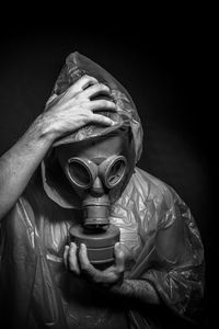 Man in raincoat wearing gas mask against black background