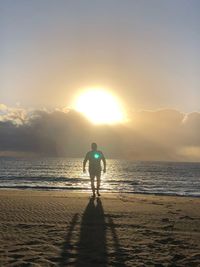 Rear view of woman on beach against sky during sunset