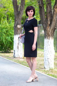 Beautiful slender middle-aged brunette in a black dress on a sunny summer day.