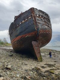 Abandoned boat on beach against sky