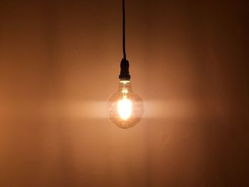 Illuminated light bulb hanging against wall