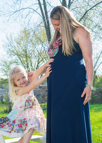 Portrait of smiling girl touching pregnant mother belly while standing outdoors