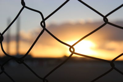 Close-up of chainlink fence against sky during sunset