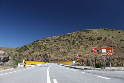 Road sign by mountains against clear blue sky