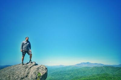 Man standing on rock against clear blue sky