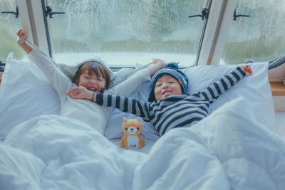 High angle view portrait of siblings with arms outstretched lying on bed at home