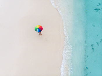 Aerial drone view of bather with colorful umbrella on the shore in maldives