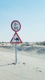 Road sign on beach against clear sky