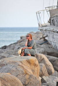 Man sitting on rock by sea against sky