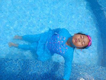 Swimming in pool. a child in a blue long-sleeved bathing suit is lying on his back in the pool.