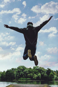 Rear view of man jumping against sky