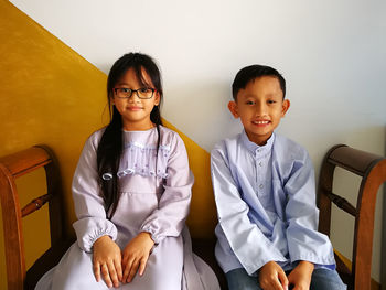 Portrait of smiling siblings sitting on bench at home during eid-ul-fitr