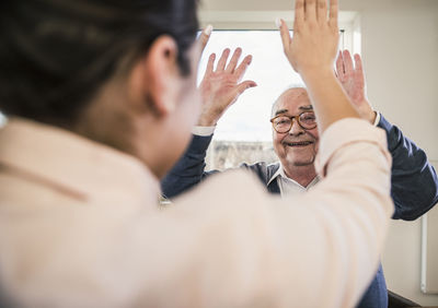 Happy senior man with raised hands looking at young woman