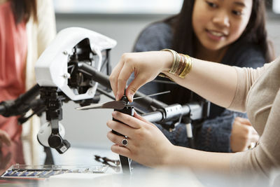 Female student fixing propeller on drone with teacher and friend in background