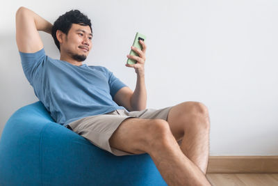 Young man using mobile phone while sitting on sofa at home