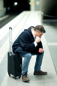 Man checking time while sitting on luggage at railroad station platform