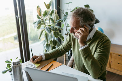 Mature man talking on mobile phone while working at home