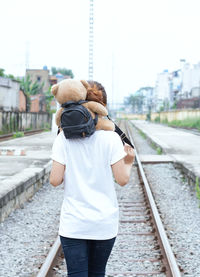 Rear view of women carrying teddy bear on railroad track