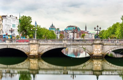 Arch bridge over river in city against sky