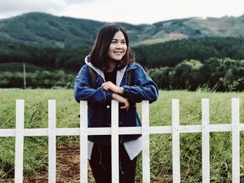 Portrait of a smiling young woman standing against fence