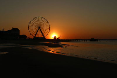 Ferris wheel at beach against sky during sunset