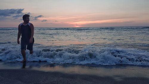 Man standing on beach against sky during sunset