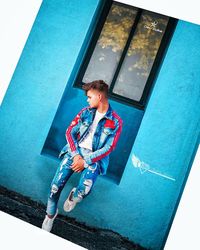 High angle portrait of boy sitting against blue wall