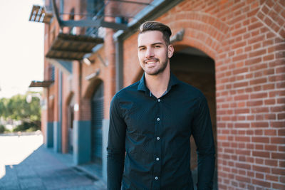 Portrait of young man standing against brick wall