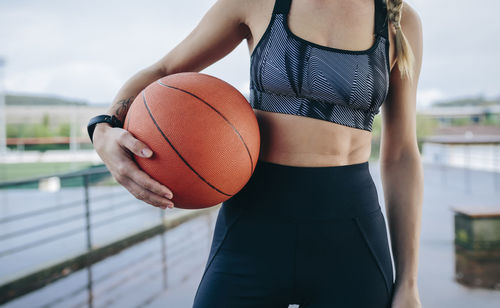 Midsection of woman holding basket ball while standing outdoors