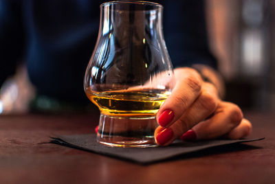 Close-up of woman holding whiskey glass on table in bar