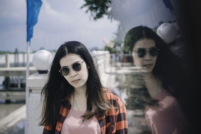 Multiple exposure of young woman wearing sunglasses standing on footpath against sky