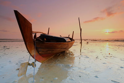 Boat moored on beach against sky during sunset
