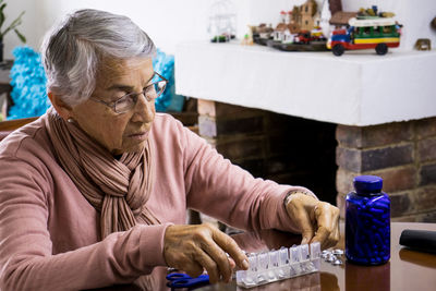 Senior woman taking medicine while sitting by table at home