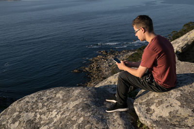 Side view of young man sitting on rock by sea