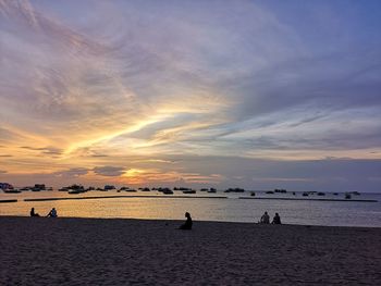 Silhouette people on beach against sky during sunset