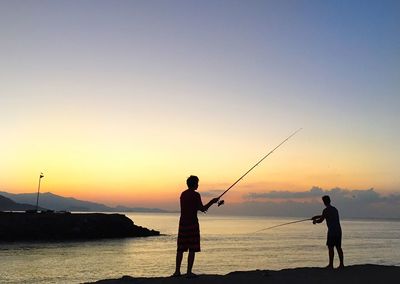 Silhouette of boys fishing on sea during sunset