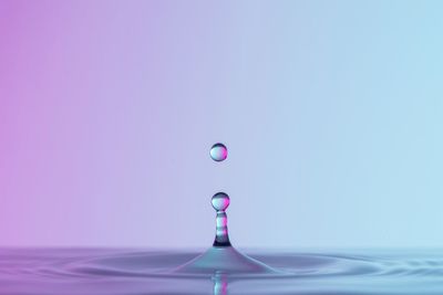 Close-up of drop falling on water against blue background