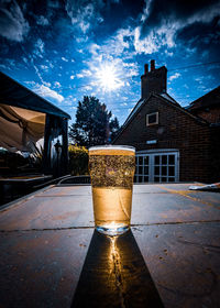 Glass of beer on building against sky in city