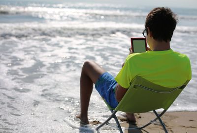 Young teenager reads a digital book on a folding chair by the sea