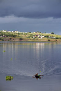 Man rowing boat in lake against sky