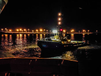 Illuminated boats moored on river in city at night