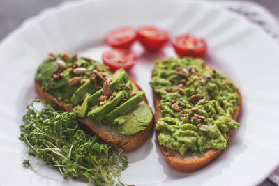 Vegan avocado sandwich with tomatoes and microgreens on a white plate on a gray background