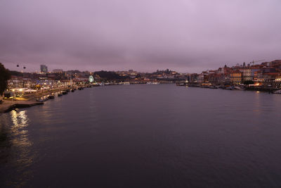 River by illuminated city against sky at dusk