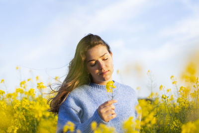 Young woman with yellow flower against sky