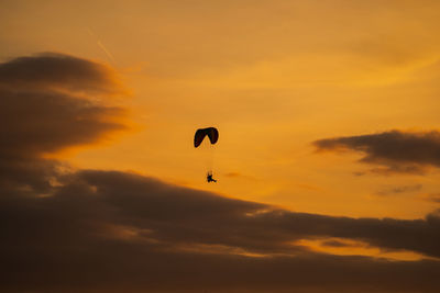 Low angle view of silhouette paragliding against sky during sunset