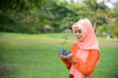 Side view of woman holding smart phone while standing on grass