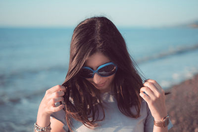 Young woman playing with hair while standing on shore at beach