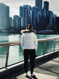 Rear view of woman standing on railing against river