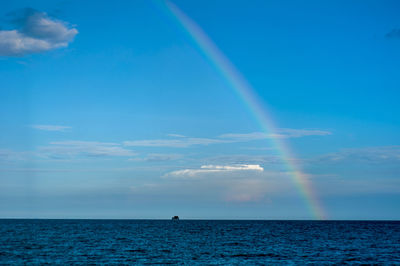 Scenic view of rainbow over sea against blue sky