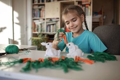 Girl holding decoration by figurine on table at home